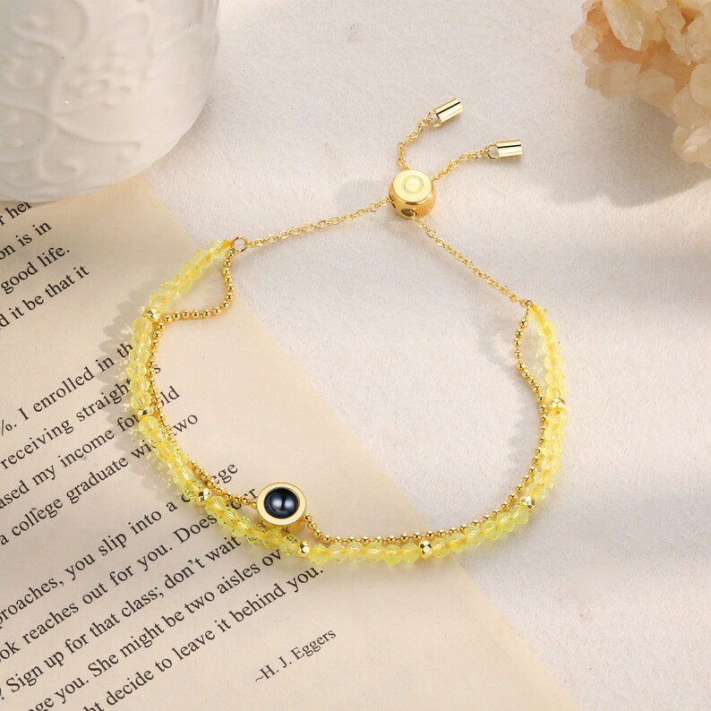 May include: A gold chain bracelet with a yellow crystal bead design. The bracelet has a sliding clasp and a small black circle charm with a gold rim.