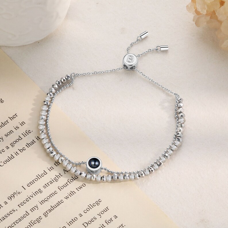 May include: A silver beaded bracelet with a black stone charm. The bracelet has a sliding clasp and is adjustable in size.