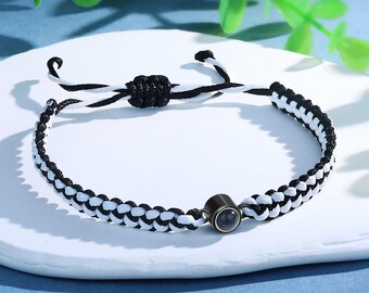 Puede incluir: Pulsera trenzada en blanco y negro con una pequeña cuenta negra en el centro.