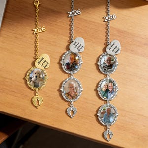 May include: Three vertical metal memorial ornaments featuring oval photo frames, silver or gold chains, and angel wing charms. The ornaments include heart-shaped tags with text reading Always in my heart, Walk with me across the stage, or Forever in my heart.