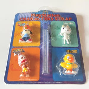 Könnte beinhalten: Eine versiegelte Packung PlayStation Characters Strap mit vier kleinen Figuren. Die Verpackung hat ein blau-weißes Design mit dem McDonald's-Logo und japanischem Text. Die Figuren umfassen einen Hund, eine Katze, einen Affen und einen gelben Vogel.