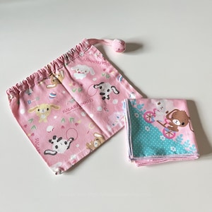Puede incluir: Bolsa rosa con cordón y tela doblada con conejitos de dibujos animados y el texto "SUGARBUNNIES". La bolsa tiene un cordón rosa con una bolita rosa. La tela tiene un estampado azul y rosa con un conejo en bicicleta.