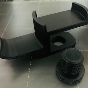 Könnte beinhalten: Schwarze, 3D-gedruckte Telefonhalterung mit gebogenem Arm und Plattform zur Aufnahme eines Telefons. Enthält einen Gewindeknopf zur Befestigung. Die Halterung ist für die Befestigung an einer Oberfläche konzipiert.