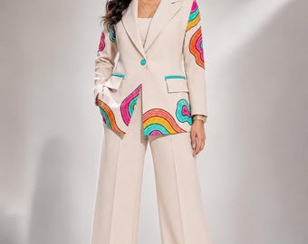 May include: A beige blazer and matching wide-leg trousers set featuring colorful, abstract, dotted patterns in shades of pink, orange, yellow, and teal. The blazer has a single teal button closure, notched lapels, and flap pockets with teal trim.