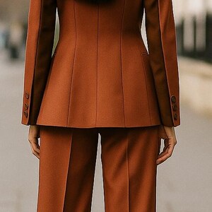 May include: A rust-colored suit, featuring a tailored blazer with three buttons on each cuff and matching wide-leg trousers. The model's back is to the camera, with long black hair.