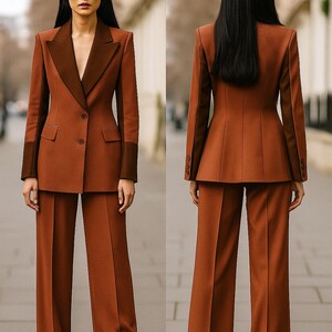 May include: A two-piece rust-colored suit with a contrasting dark brown lapel and sleeve cuffs. The suit features a tailored blazer with a two-button closure and wide-leg trousers. The model is standing on a paved surface.
