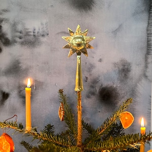 Può includere: Un piccolo albero di Natale decorato con fette di arancia essiccate e candele accese. Una stella dorata si trova in cima all'albero.