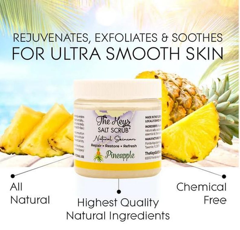 Puede incluir: Un tarro de exfoliante de sal The Keys con etiqueta "Pi&ntilde;a", rodeado de rodajas de pi&ntilde;a fresca. El texto dice "Rejuvenates, Exfoliates & Soothes For Ultra Smooth Skin." El texto adicional incluye "All Natural" y "Chemical Free."