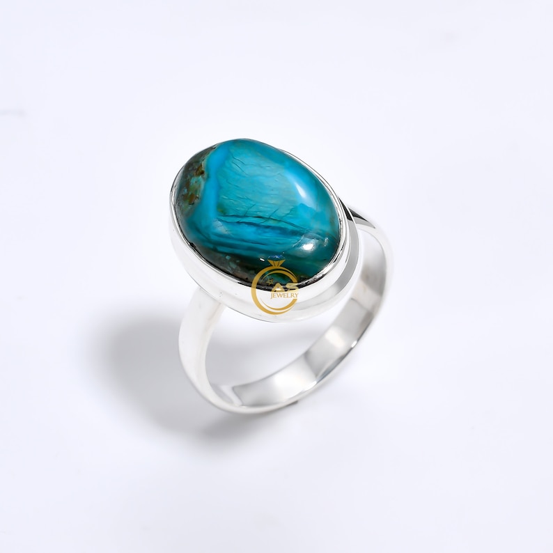 May include: A silver ring with a large oval turquoise gemstone. The gemstone has a blue and green color with a swirling pattern.