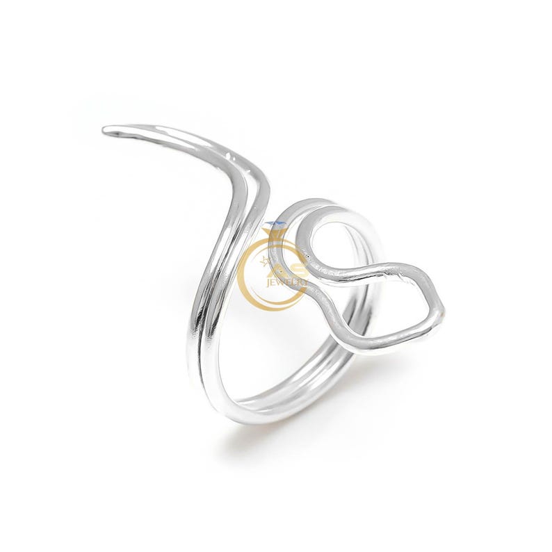 May include: A silver-colored ring with a unique, abstract design. The ring features a curved, wave-like shape that wraps around the finger, with a loop and a pointed end. The jewelry is set against a white background.