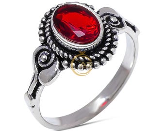 Puede incluir: Anillo de plata con una gema roja ovalada. La gema está engastada en un bisel ornamentado con un borde de cuentas. La banda del anillo tiene un diseño simple y pulido con adornos decorativos a ambos lados de la gema.