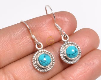 May include: A pair of silver dangle earrings with turquoise stones set in a circular design. The earrings have a simple hook closure.