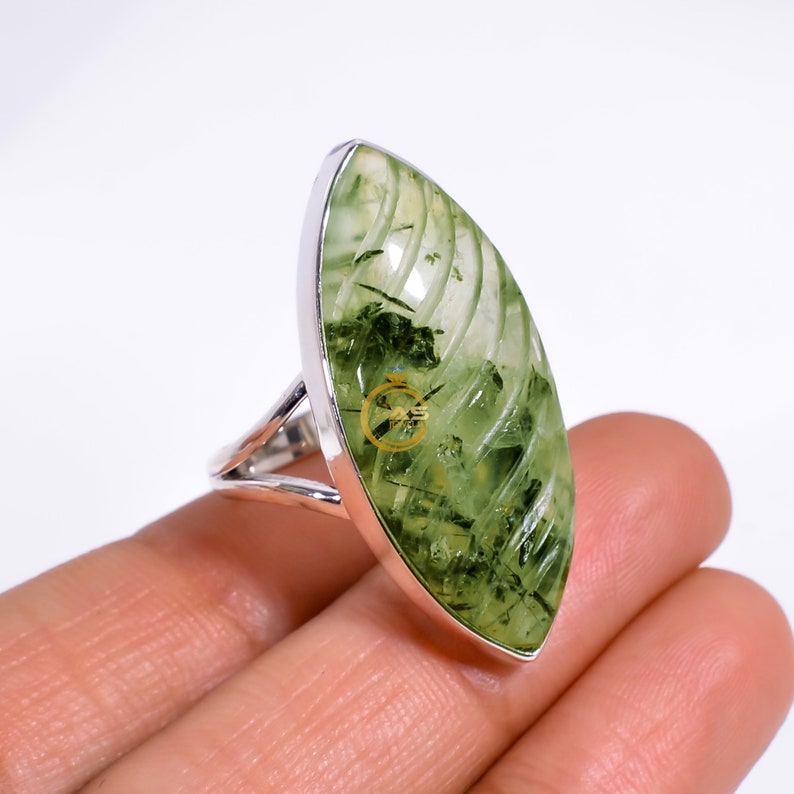 Puede incluir: Un anillo de plata con una piedra preciosa de aventurina verde. La piedra tiene forma de marquesa y presenta un patr&oacute;n de remolino.