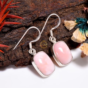 Può includere: Un paio di orecchini d'argento con pietre di opale rosa. Gli orecchini hanno una forma rettangolare e sono incastonati in una cornice d'argento.