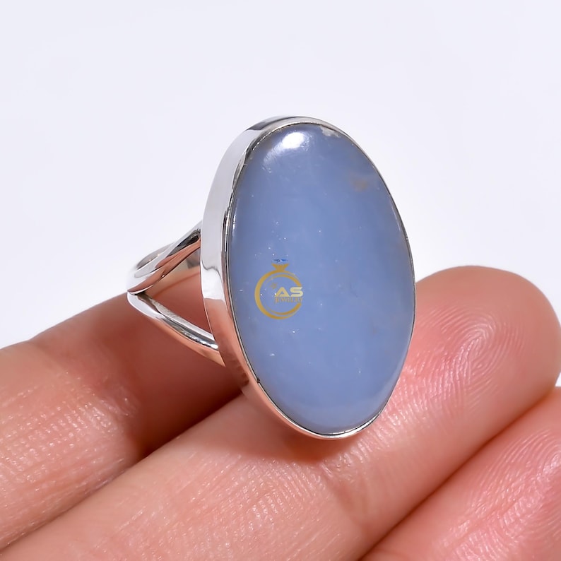 May include: A silver ring with a large oval blue chalcedony gemstone. The ring has a simple band with a split shank.