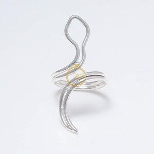 May include: A silver-colored ring with a unique, abstract design. The ring features a swirling band that wraps around the finger, with an elongated, curved element extending upwards. The ring is set against a white background.