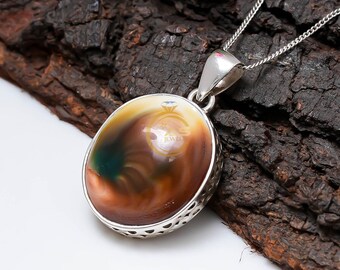 May include: Oval pendant necklace with a silver chain. The pendant features a polished, multicolored stone with shades of brown, tan, and green, set in a decorative silver bezel. The necklace is displayed on a dark, textured background.