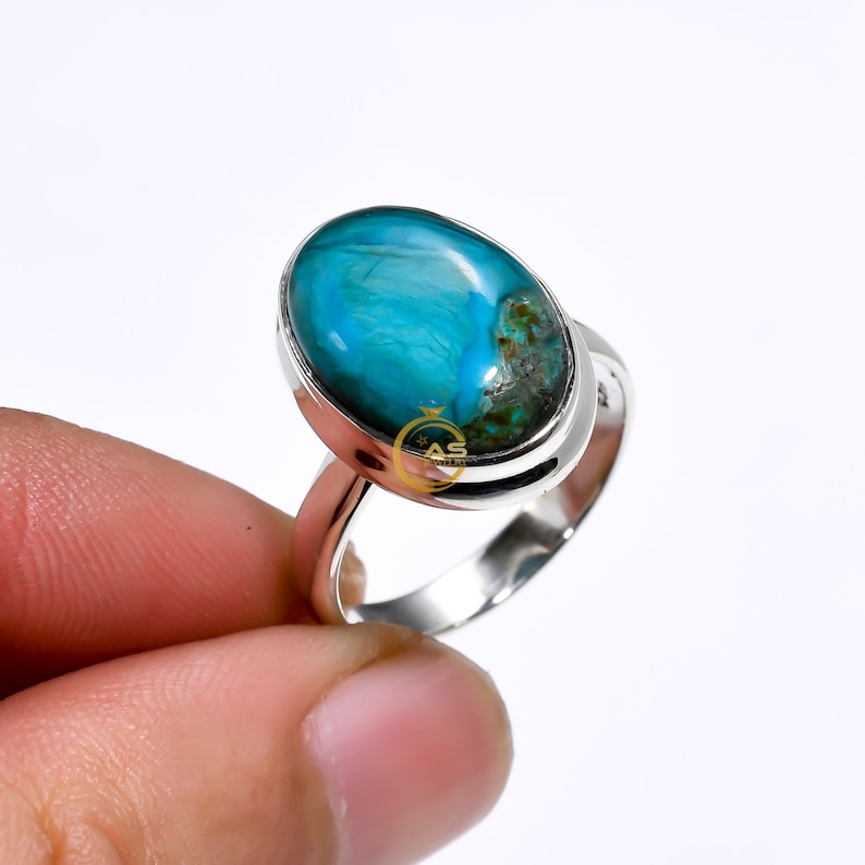 May include: A silver ring with a large oval turquoise gemstone. The gemstone has a blue and green color with a swirling pattern.