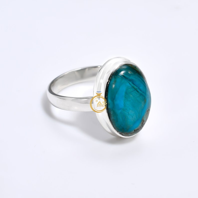 May include: A silver ring with a large oval turquoise gemstone. The gemstone has a blue and green color with a marbled pattern.