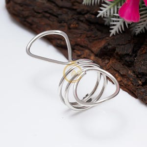 May include: A silver-colored napkin ring with a unique design. The ring features a looped structure with a handle, creating an elegant and modern look. The napkin ring is made of a shiny, reflective metal.