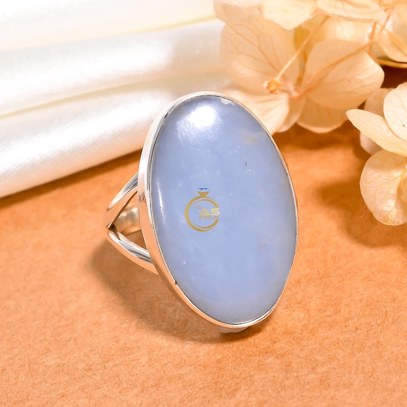 May include: A silver ring with a large oval-shaped blue gemstone. The ring has a simple design with a smooth band.