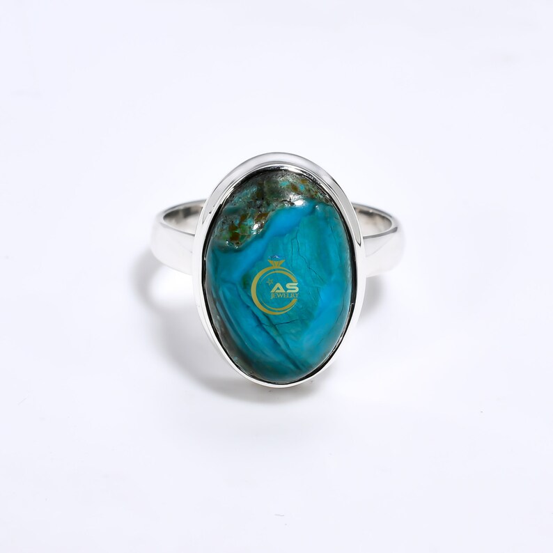 May include: A silver ring with a large oval turquoise gemstone. The gemstone has a blue and green color pattern.