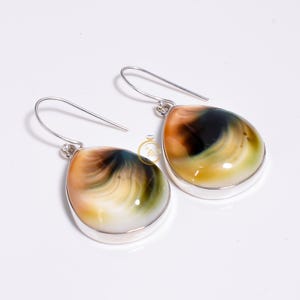 May include: A pair of teardrop-shaped earrings featuring polished, multi-colored stones with swirling patterns of cream, amber, dark brown, and olive green. Each stone is set in a smooth silver bezel and hangs from a simple silver hook.
