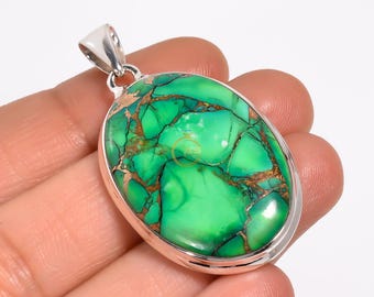 May include: Oval-shaped pendant with a vibrant green and gold stone set in a silver-colored metal. The stone has a unique, marbled appearance with a polished finish. The pendant has a simple, elegant design, suitable for everyday wear.