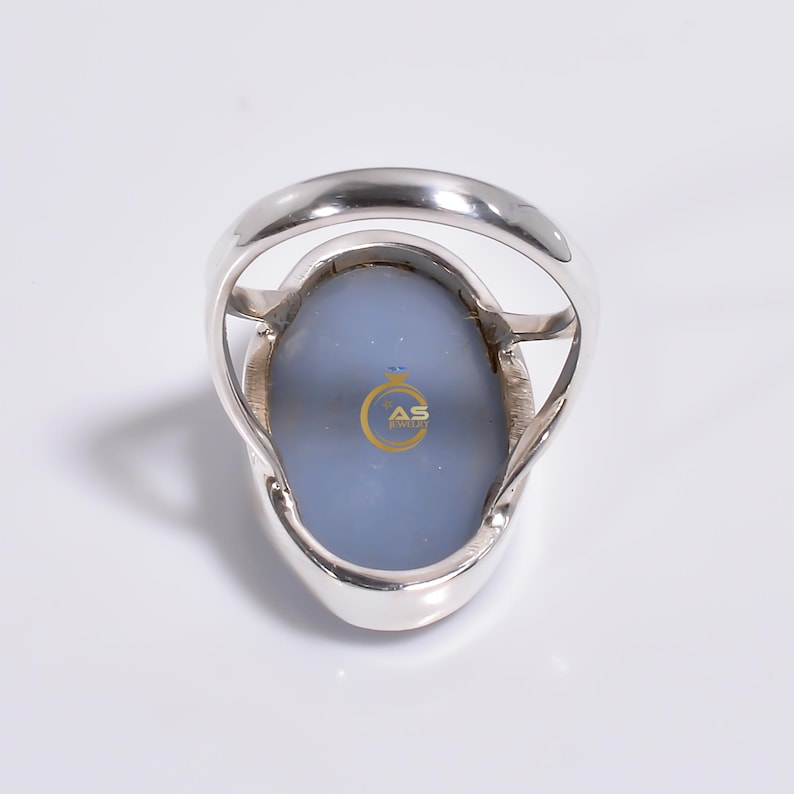 May include: A silver ring with a large oval blue agate stone. The ring is set in a silver band with a simple design. The back of the ring has the words "AS Jewelry" engraved on the stone.
