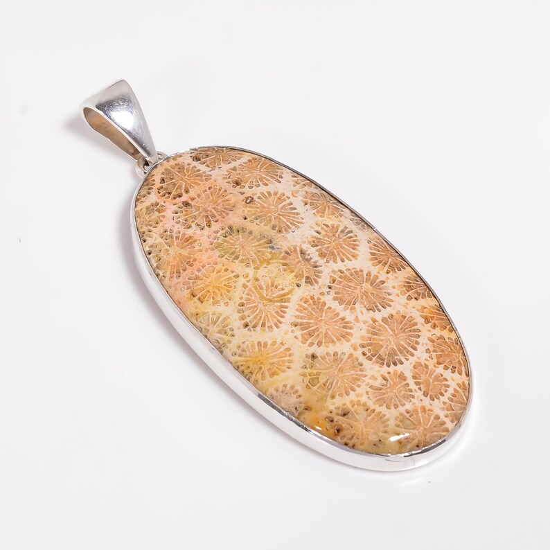 Peut inclure: Un pendentif en argent avec une incrustation ovale de corail fossilis&eacute; brun clair. Le corail pr&eacute;sente un motif d&eacute;taill&eacute; de petites formes de fleurs blanches.