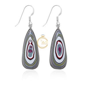 May include: A pair of teardrop-shaped drop earrings featuring layered, multi-coloured Fordite patterns in white, red, blue, yellow, and grey. The earrings hang from silver-toned hooks and include a logo with the text AS JEWELRY.