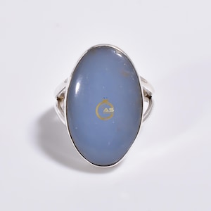 May include: A silver ring with a large oval blue chalcedony gemstone. The ring has a simple band with a slightly curved design.