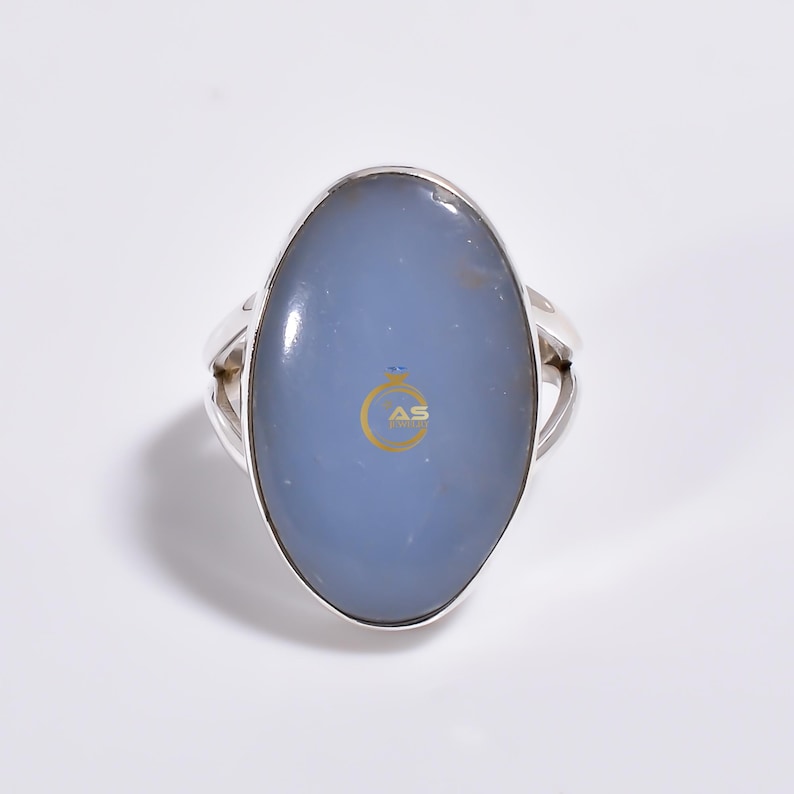 May include: A silver ring with a large oval blue chalcedony gemstone. The ring has a simple band with a slightly curved design.
