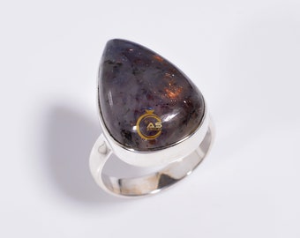 Può includere: Un anello d'argento con una pietra preziosa iridiscente a forma di lacrima. La pietra preziosa è di colore viola scuro e rame.