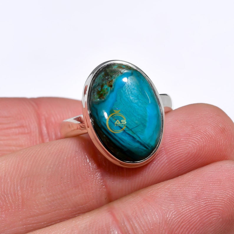 May include: A silver ring with a large oval turquoise gemstone. The gemstone has a blue and green color with a swirling pattern.
