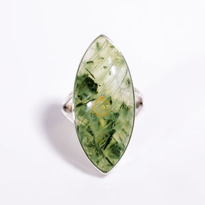 Puede incluir: Un anillo de plata con una piedra preciosa verde, de forma marquesa, con vetas marmoleadas.