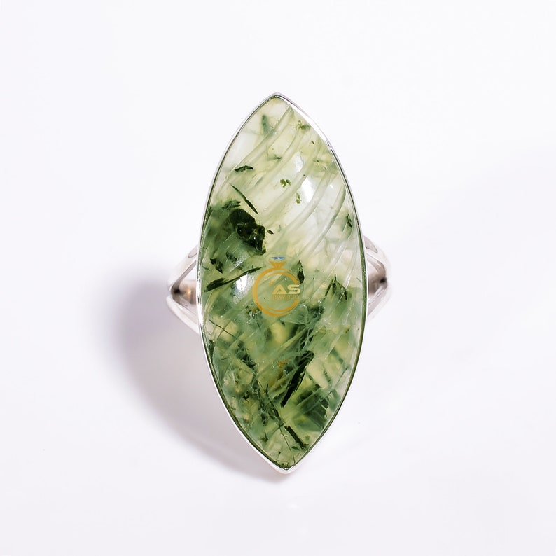 Puede incluir: Un anillo de plata con una piedra preciosa verde, de forma marquesa, con vetas marmoleadas.