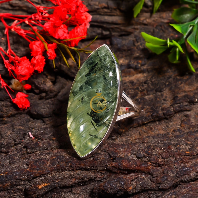 Puede incluir: Un anillo de plata con una piedra preciosa ovalada de color verde. La piedra preciosa tiene un patr&oacute;n estriado y un centro verde oscuro.