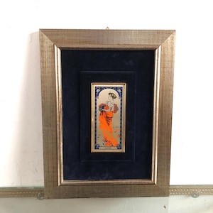 May include: A framed art print featuring a woman in a red dress holding flowers. The print is set against a blue velvet background and has a gold frame.