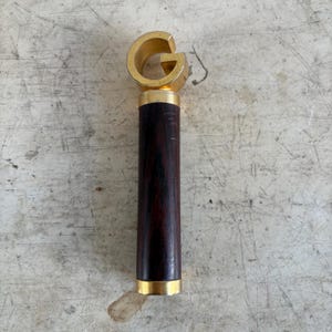 May include: A bottle opener featuring a gold-coloured "G" design. It has a dark brown wooden handle with gold accents. The opener is approximately 15 cm long. A stylish barware accessory.