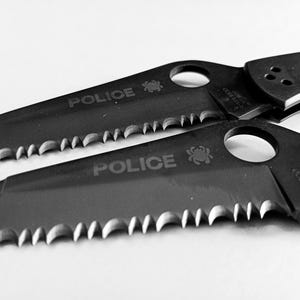 May include: Two black folding knives with serrated blades and the word "POLICE" engraved on the handles.