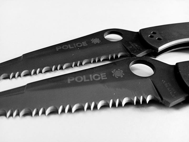 May include: Two black folding knives with serrated blades and the word "POLICE" engraved on the handles.