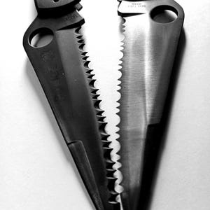 May include: Two black pocket knives with serrated blades and a hole in the handle. The blades are partially open and the handles are closed.
