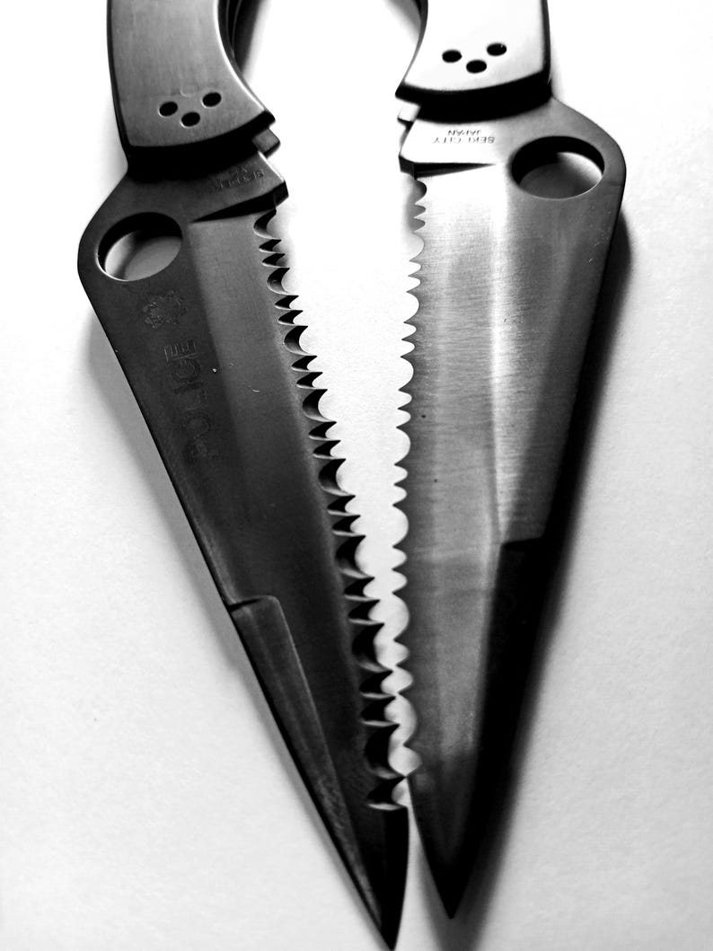 May include: Two black pocket knives with serrated blades and a hole in the handle. The blades are partially open and the handles are closed.