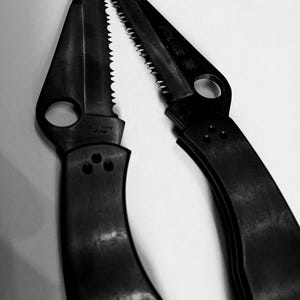 May include: A black folding knife with a serrated blade and a "POLICE" inscription. The knife has a black handle and a silver metal clip.