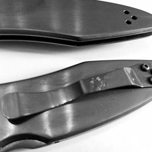 May include: Two black pocket knives with a silver clip and a silver pocket clip. The top knife has a row of three small holes on the handle. The bottom knife has four small holes on the handle.