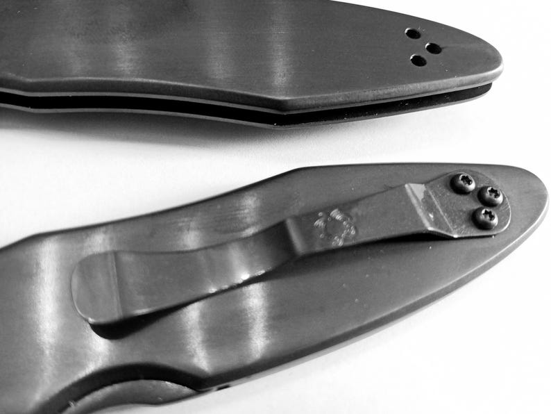 May include: Two black pocket knives with a silver clip and a silver pocket clip. The top knife has a row of three small holes on the handle. The bottom knife has four small holes on the handle.