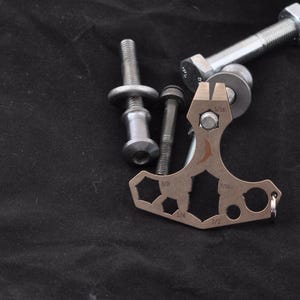 Könnte beinhalten: Ein silbernes Multitool mit verschiedenen Größen von Inbusschlüsseln und einem Flaschenöffner. Das Werkzeug ist aus Metall und hat eine silberne Oberfläche. Das Werkzeug liegt auf einer schwarzen Oberfläche.