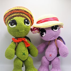 Peut inclure: Deux peluches de tortues au crochet, une verte avec un chapeau rayé multicolore et une écharpe orange, et une violette avec un chapeau jaune et des fleurs roses.