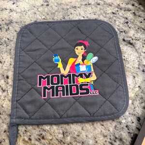May include: Gray quilted pot holder with a loop for hanging. The pot holder features a graphic of a woman holding cleaning supplies, with the text "MOMMY MAIDS LLC" in pink and black.